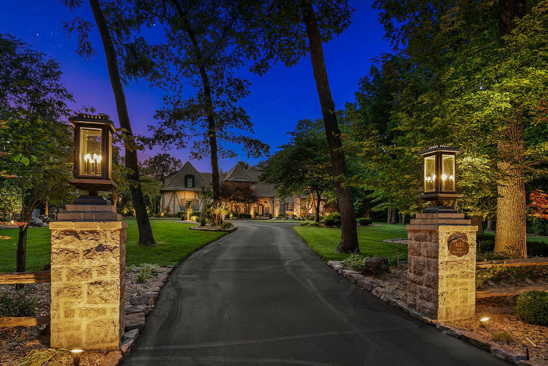 two outdoor lights illuminating drive path towards large house
